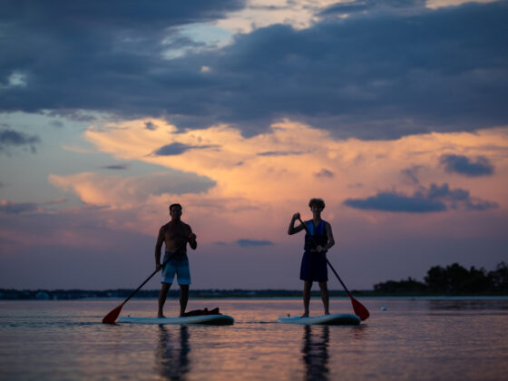 Photograph of father and son paddle boarding during a sunset on Pensacola Beach, FL.